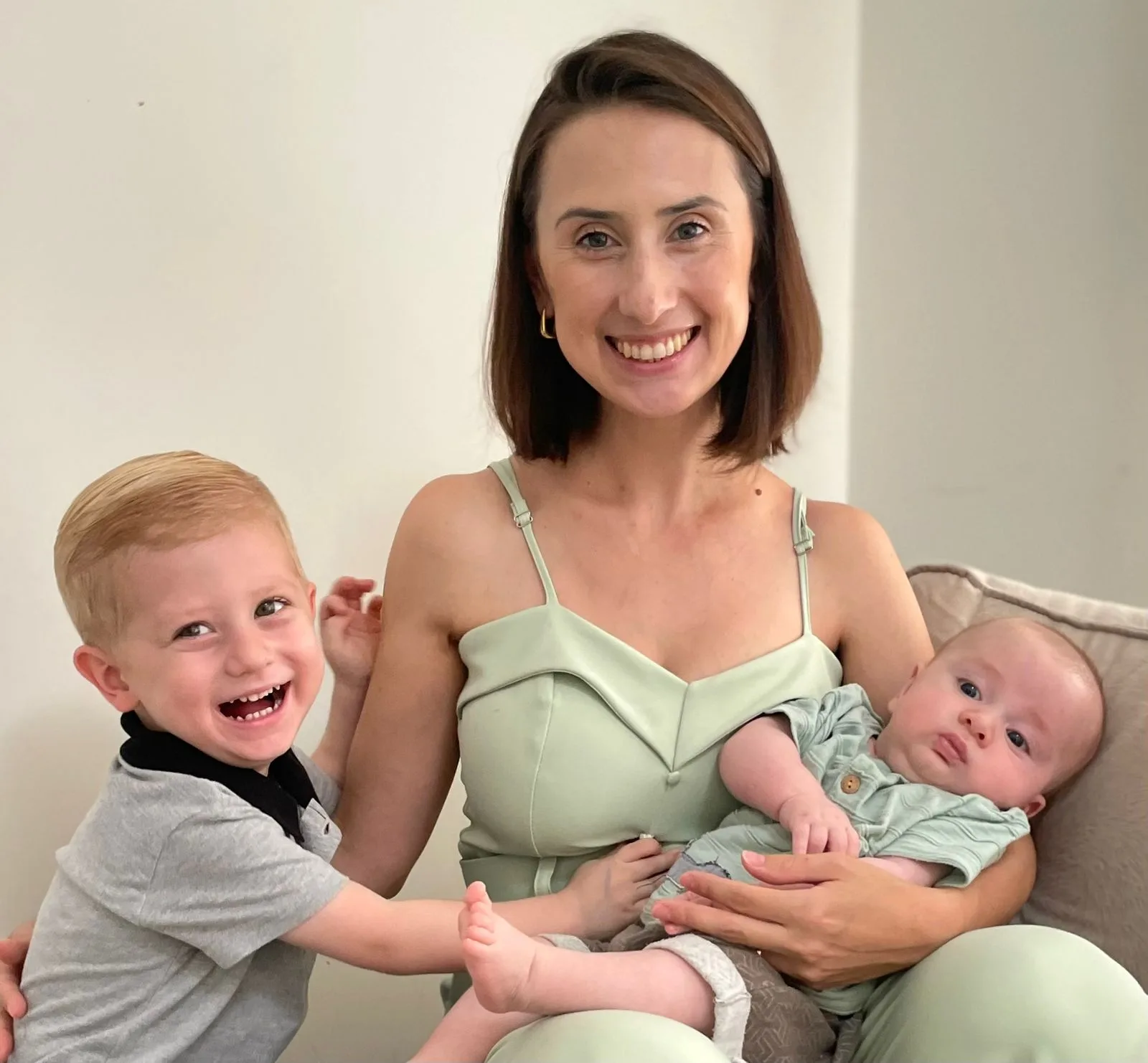 A Thalita Muller, branca de cabelo liso nos ombros, com seus dois filhos no colo.