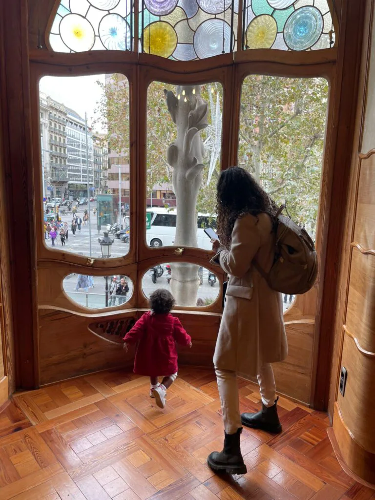 Uma mulher com mochila e a filha correndo, em direção a janela, dentro da casa Batlò, em Barcelona.