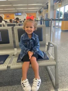 Menina pequena com laço laranja no aeroporto 