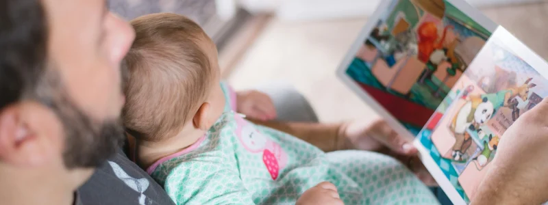Pai lendo um livro ilustrado para seu bebê no colo, aproveitando o conforto e a tranquilidade de uma casa inteligente.